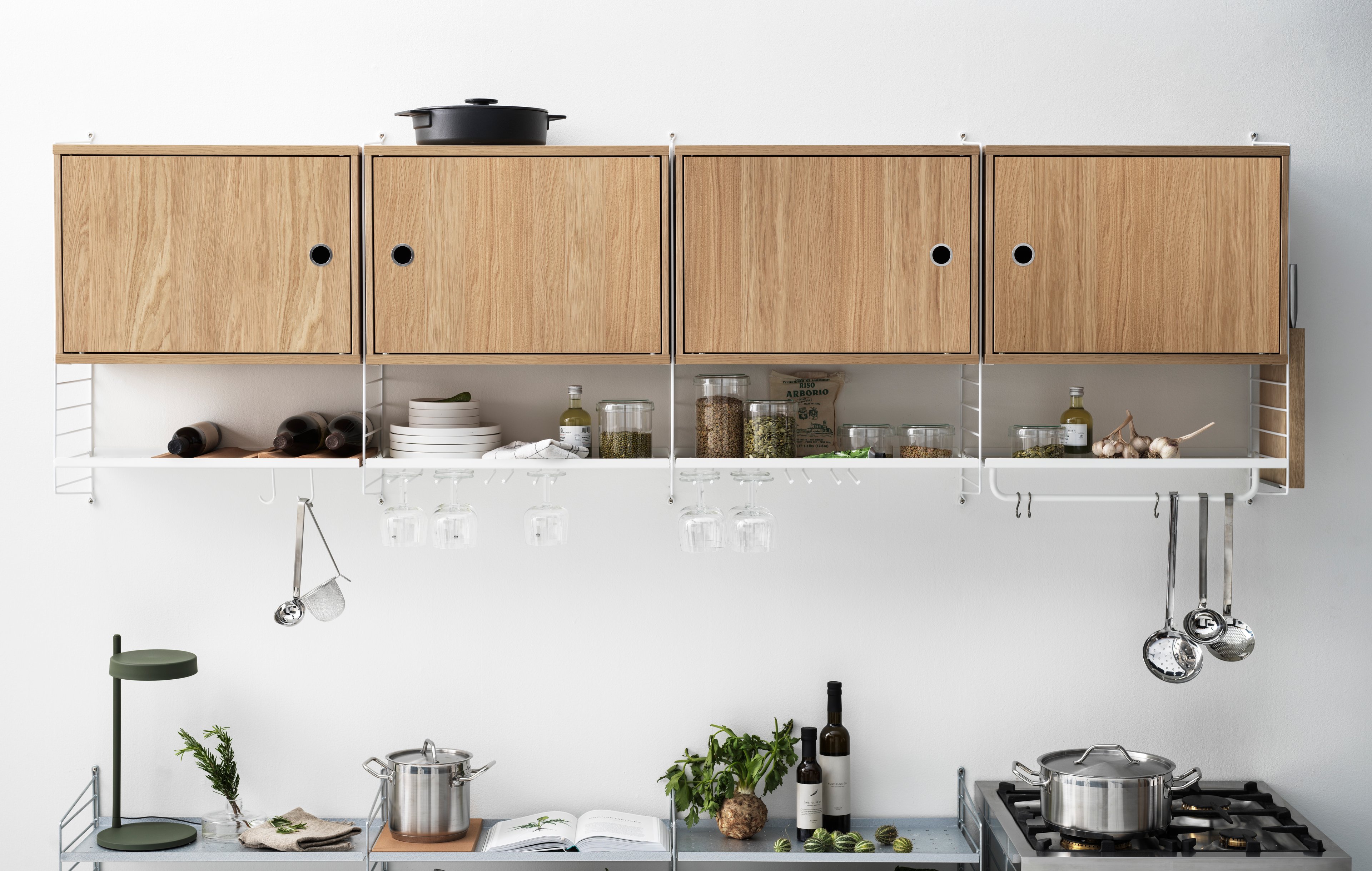 String shelf with wall panels and metal shelves with low edge along with cabinets with swing door and a rod. This wall-hung shelving combination is perfect for a kitchen. Place it close to the oven for easy access to all kitchen tools.