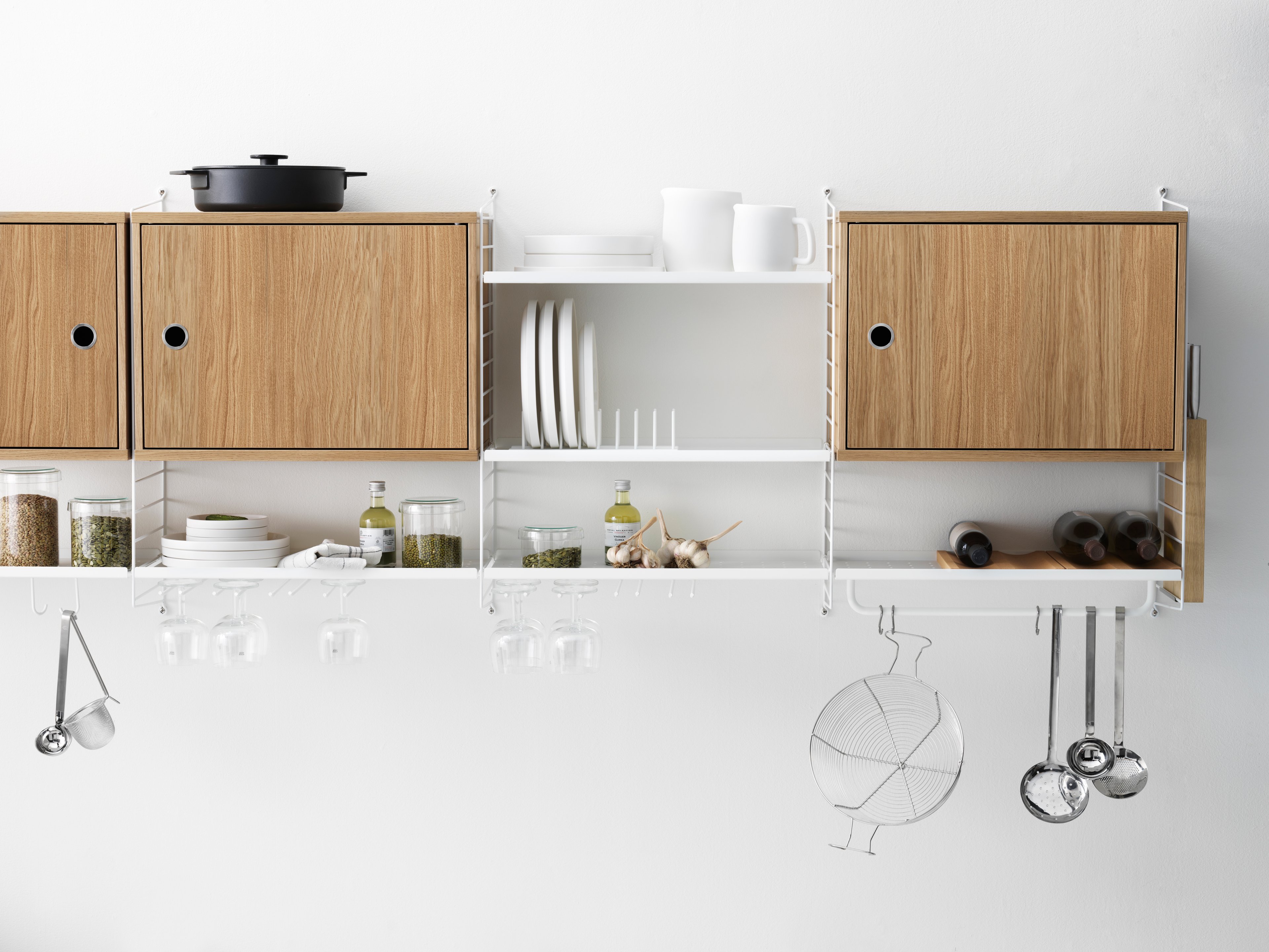 String shelf with wall panels and metal shelves with low edge along with cabinets with swing door and a rod. This wall-hung shelving combination is perfect for a kitchen. Place it close to the oven for easy access to all kitchen tools.